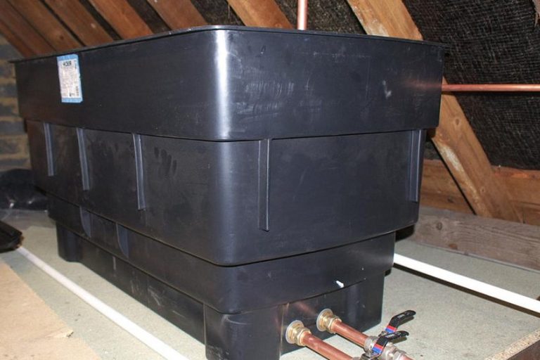 Large black plastic water tank situated in an attic, with visible copper piping.